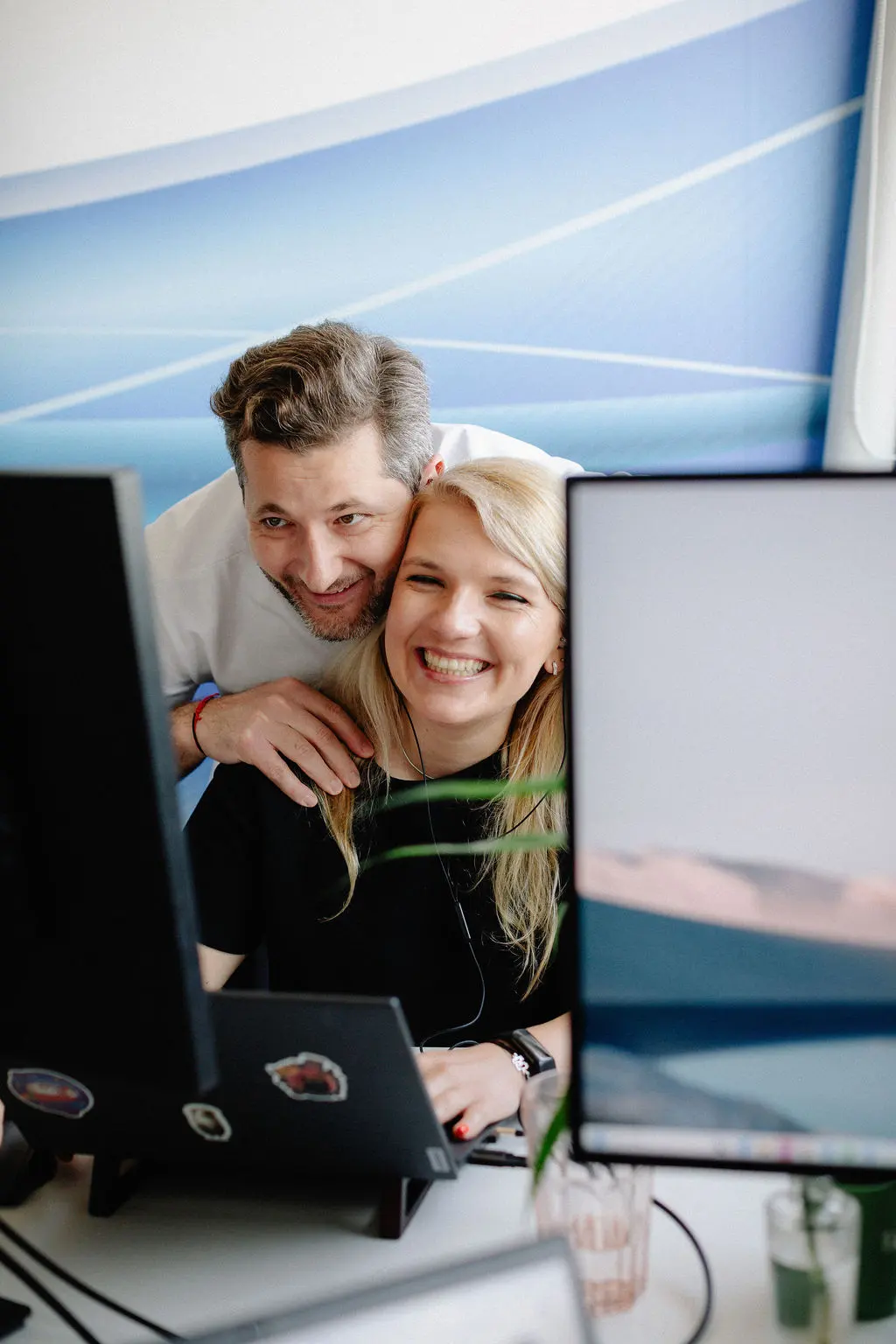 Two colleagues smiling at a monitor